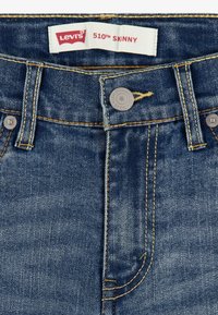 Vaqueros ajustados Levi's 510 en denim azul oscuro, con costuras doradas, botón metálico y etiqueta de marca. La tela muestra ligeras decoloraciones y textura.
