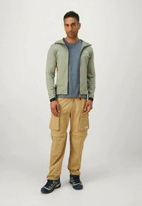 Vaaleanharmaa vetoketjullinen huppari, sininen t-paita, vaaleat cargo-housut taskuilla ja tummat kengät. Suora rakenne ja rento urheilullinen istuvuus.