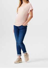 Lyserød, kortærmet V-hals top, parret med blå denimjeans. Beige sneakers med lyse detaljer og opsmøgede bukseben fuldender outfittet.
