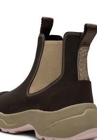 Botín impermeable marrón hasta el tobillo con paneles laterales elásticos en color beige, acentos texturizados marrones y una suela gruesa en beige. Presenta un detalle en el talón tejido.
