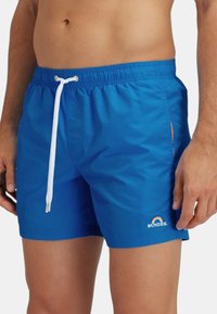 Pantaloni da bagno blu realizzati in materiale leggero, con un cordoncino bianco, tasca laterale e un piccolo logo con un accento arcobaleno.