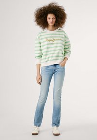 Sweatshirt a righe verde e bianche con logo dorato, abbinato a jeans azzurri e sneakers bianche. Tessuto morbido e vestibilità casual.