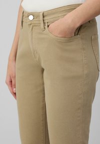 Pantaloni khaki con taglio aderente, dotati di una semplice chiusura con bottone e tasche laterali, realizzati in un tessuto liscio e resistente.
