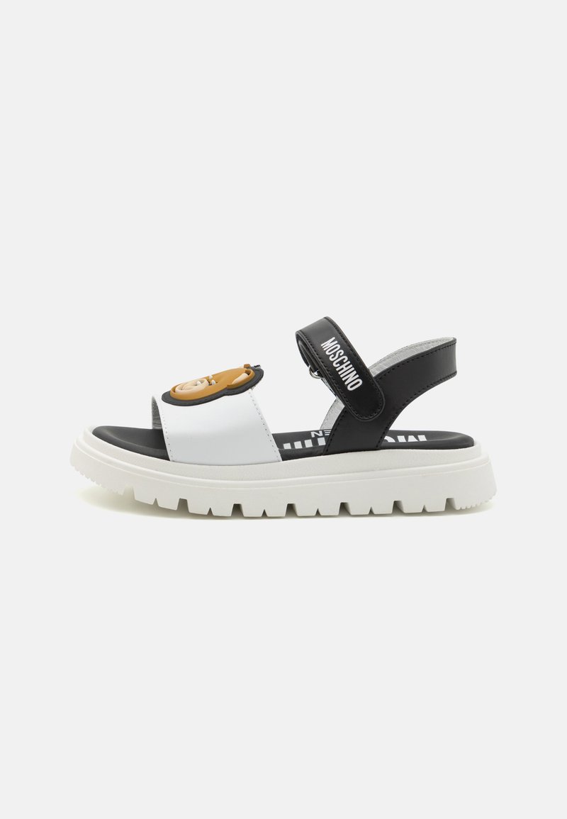 Sandalias en blanco y negro con una suela gruesa, que presentan un gráfico de dibujos animados en la correa delantera y una correa ajustable en el tobillo negra.