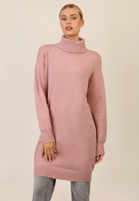 Rosa oversized Pullover mit einem hohen, gerippten Kragen und langen Ärmeln. Weicher, strukturierter Stoff mit einer lässigen Passform, kombiniert mit grauen Jeans.