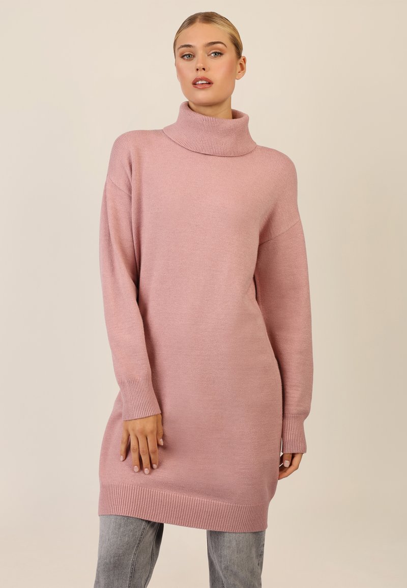 Rosa oversized sweater med høj, ribbet hals og lange ærmer. Blødt, tekstureret stof med en afslappet pasform, parret med grå jeans.