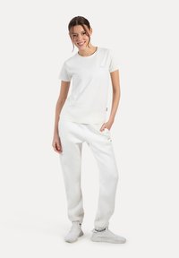 Hvid bomulds t-shirt med kortærmer og et lille logo, parret med hvide løse sweatpants og hvide sneakers.