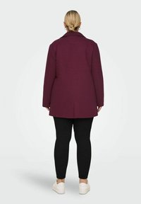 Manteau bordeaux avec un design structuré, featuring un col cranté, des coutures d'épaule et une coupe droite. Associé à des leggings noirs et des baskets blanches.