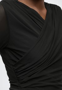 Μαύρο τοπ με σχεδιασμό τύπου κρουαζέ και ριχτό, με υφή στο ύφασμα. Ο λαιμός συγκεντρώνεται, προσθέτο�ντας βάθος στο λείο υλικό.