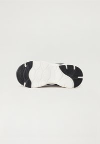 Czarnobiała podeszwa sportowego buta, z wzorowanym bieżnikiem, teksturowanymi powierzchniami i zakrzywionym kształtem dla lepszej przyczepności i trwałości.