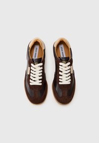 Pruunid samet- ja nahksneakerid valgete paeltega, ümmarguse varbaga ja beežide aktsentidega; omavad pehmet kaelust ja logode detailimist.