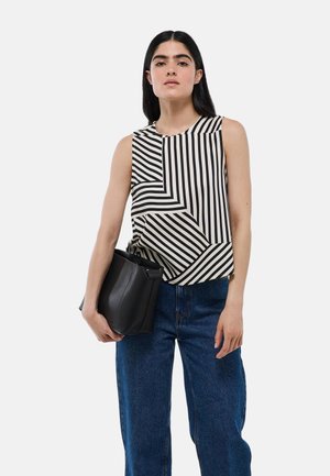 Haut sans manches avec des rayures noires et blanches audacieuses dans un motif géométrique, associé à un jean bleu taille haute et un sac en cuir noir.