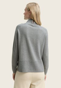 Grauer Strickpullover mit hohem Kragen und Rückenschlitz. Hat lange Ärmel, gerippten Saum und eine weiche Textur.