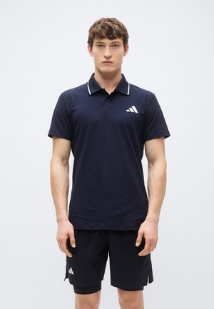 Polo bleu marine avec bordure blanche et logo à trois bandes sur la poitrine, associé à un short noir présentant un logo similaire sur le côté.