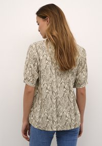 Top beige a maniche corte con un motivo marrone a vortice, dalla vestibilità morbida e orlo arrotondato, realizzato in tessuto leggero.
