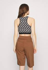 Czarny sportowy biustonosz z powtarzającym się wzorem białego tekstu, w połączeniu z brązowymi, dopasowanymi szortami z tylnymi kieszeniami i krótkim krojem.