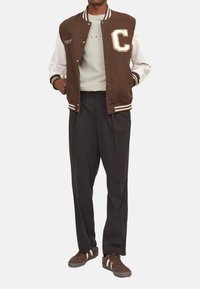 Brun uldblandings varsity jakke med hvide læderærmer, med et stort "C" emblem, parret med mørke tapered bukser og brune sneakers.