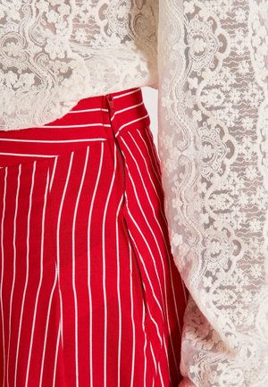 Jupe rayée rouge et blanche avec une fermeture éclair sur le côté, assortie à un blouse en dentelle blanche avec des motifs floraux et des détails texturés.