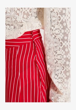 Falda a rayas rojas y blancas con cremallera lateral, combinada con una blusa blanca de encaje con patrones florales y detalles texturizados.