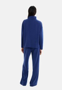 Niebieski, ciężki zestaw dresowy z polaru, składający się z długiego rękawa z wysokim kołnierzem oraz luźnych spodni o szerokich nogawkach. Gładka faktura.