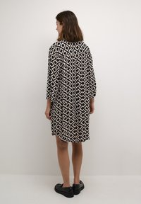 Black and cream patterned shirt dress with geometric diamond shapes, three-quarter sleeves, and a loose fit, paired with black shoes.