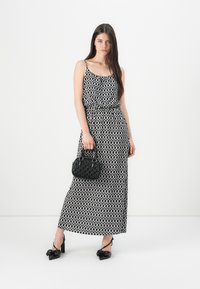 Abito lungo con motivo geometrico bianco e nero, spalline sottili, vita cintrata e gonna fluida; abbinato a una borsa nera e tacchi.