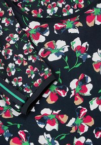 Tessuto con motivo floreale caratterizzato da grandi fiori bianchi, rosa e verdi su uno sfondo blu scuro; include un accento di bordo nero solido.