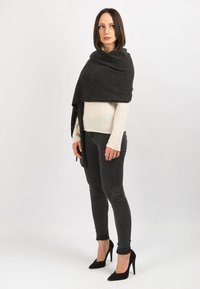 Uldne sort sjal lagt over en lysblå top, parret med mørke skinny jeans og sorte højhælede sko. Glat tekstur, enkelt design.