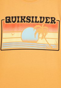 Camiseta amarilla con un diseño gráfico que incluye el texto "QUIKSILVER", un sol, una palmera, aves y bandas de color superpuestas en naranja, azul y beige.