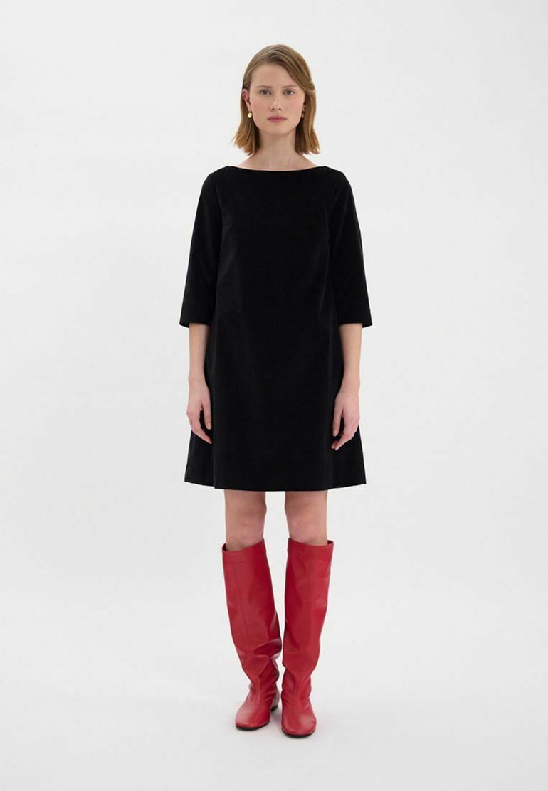 Robe A-line en velours noir avec des manches trois-quarts, associée à des bottes en cuir rouges jusqu'aux genoux. Design simple, longueur au genou, accents minimalistes.