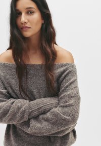 Off-shoulder, chunky knit sweater in a grey-brown color, featuring a textured pattern and ribbed cuffs, with loose, relaxed fit.