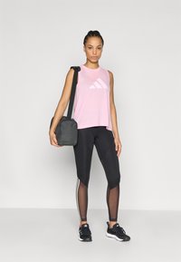 Ροζ αμάνικο αθλητικό τοπ με λευκό λογότυπο, μαύρο κολάν με πλέγμα, και μαύρα αθλητικά παπούτσια. Casual μαύρη τσάντα χιαστί.