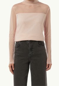 Helles rosa Netzoberteil mit langen Ärmeln und transparenter Halslinie, verziert mit verstreuten Funkeln. Kombiniert mit hochgeschnittenen schwarzen Jeans.
