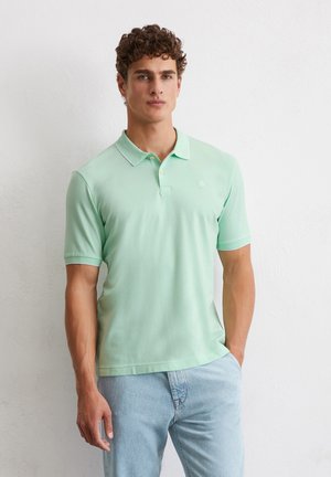 Light green polo shirt with a classic collar, short sleeves, and two-button placket; smooth fabric; logo on the chest; worn with light blue jeans.