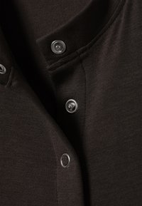 Detailný záber na čiernu tkaninu s tromi striebornými patentkami na otvore odevu.