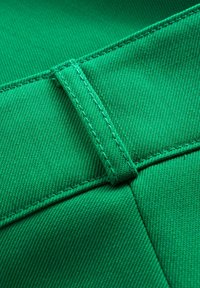 Groene stofdetail met een gladde textuur, voorzien van versterkte stiksels en een taillebandaccent voor structurele ondersteuning.