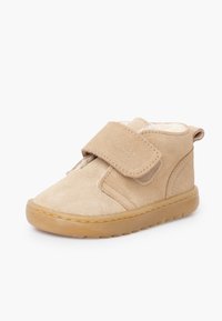 Botín beige de ante con una correa de velcro, forro interior suave, punta redonda y suela de goma texturizada. Diseño sencillo sin patrones.