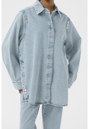 Jasnoniebieska kurtka dżinsowa z kołnierzem, zapinana na guziki z przodu, ozdobiona srebrnymi guzikami na rękawach dla dodatkowego efektu.