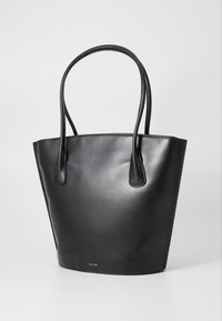 Sac tote en cuir noir avec deux longues poignées, forme effilée, texture lisse et détail de logo doré proéminent en bas.