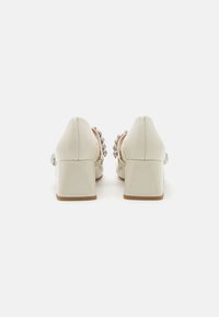 Scarpe con tacco alto beige con finitura lucida, dotate di un tacco quadrato e di una fascia decorata con gruppi di gemme trasparenti.