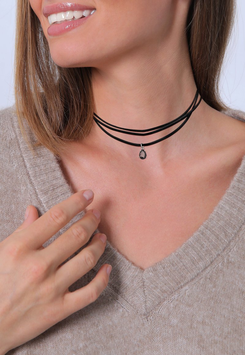 Black multi-layer choker with three strands and a small teardrop pendant. Soft texture and simple design, worn against a light sweater.