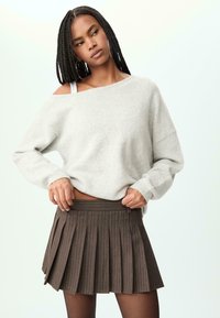 Svijetlosiva oversized sweatshirt sa širokim izrezom, uparena s smešnom mini suknjom s plisama koja ima suptilne vertikalne pruge.