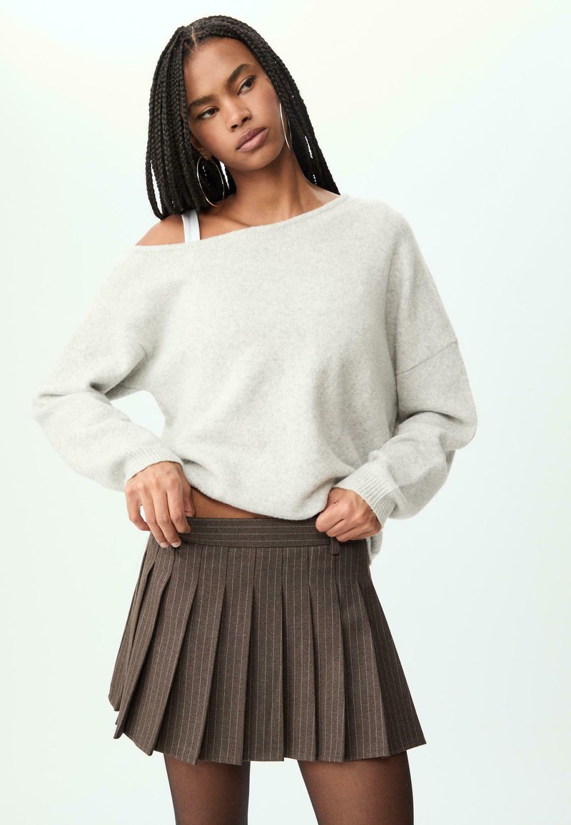 Svijetlosiva oversized sweatshirt sa širokim izrezom, uparena s smešnom mini suknjom s plisama koja ima suptilne vertikalne pruge.