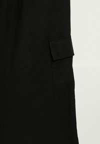 Černý oděv z látky s kapsou na boku. Hladká textura a jednoduchý design bez ozdob.