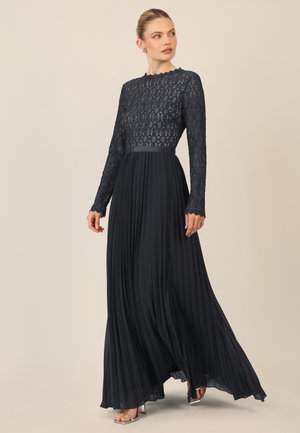 Langes, dunkelnerviges Kleid mit einem strukturierten Spitzen-Oberteil im Diamantmuster, langen Ärmeln und einem gefältelten Rock. Satinschärpe als Detail.