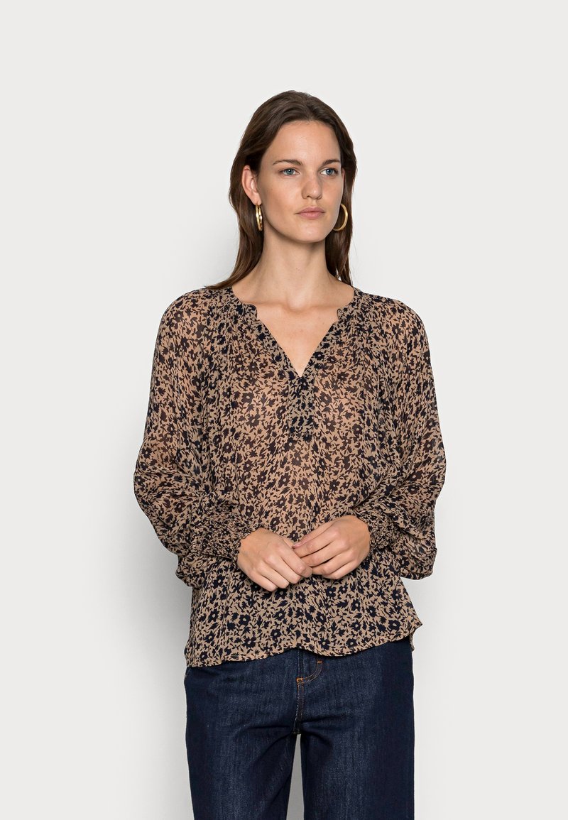 Blusa de manga longa em tecido leve e transparente com padrão floral castanho, decote em V, e punhos elásticos, combinada com jeans escuros.