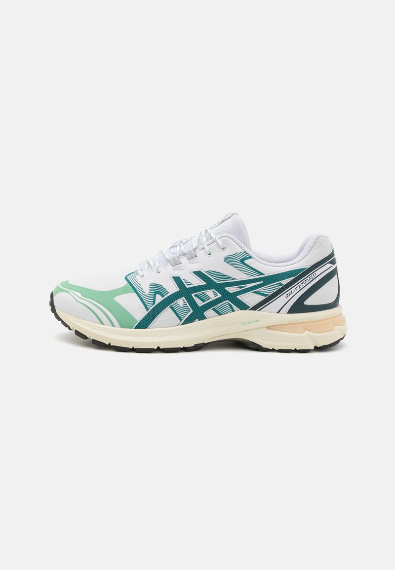 Sapatilha de corrida em branco com detalhes em verde e azul-marinho. Apresenta um cabedal respirável, sola texturizada e um meio-solo acolchoado para suporte.