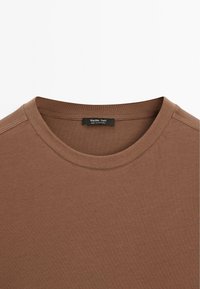 T-shirt marron à col rond avec des coutures visibles et une étiquette noire au niveau du cou indiquant "Massimo Dutti Made in Portugal."