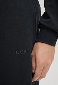 Czarna bawełniana bluza z subtelnie wytłoczonym logo "JOOP!" po lewej stronie. Tkanina ma gładką strukturę i luźny krój.
