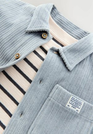 Gray corduroy shirt with a buttoned collar. Underneath, a pink and black striped shirt. Textured fabric with visible stitching and tags.